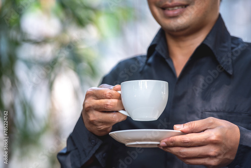 Asian man holding hot coffee in paper mug cup to sniff smell of espresso in morning sunlight. man carry coffee break to sniff fragrant smell the aroma of coffee and work.
