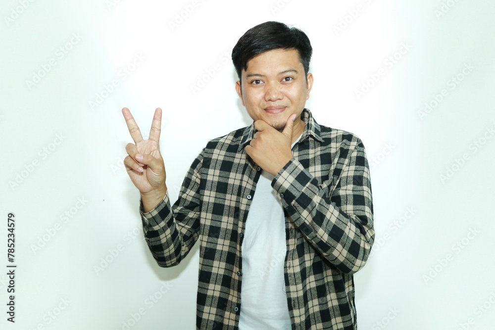Young Asian man shows a curious facial expression while giving the two finger sign Young Asian man shows a curious facial expression while giving the two finger sign