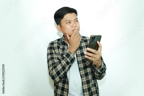 Young Asian man thinking about something while holding a mobile phone photo
