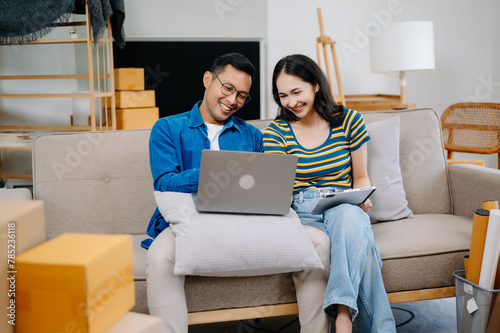 Asian young attractive couple man and woman use tablet and smartphone online shopping furniture decorate house with carton package move in new house.