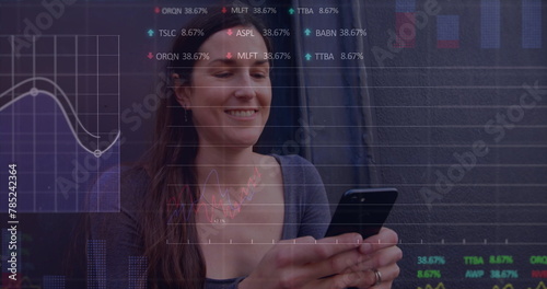 Image of multiple graphs and trading boards, caucasian woman sitting and using smartphone