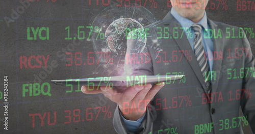 Image of financial data processing and globe over businessman holding tablet