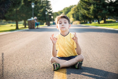 A boy is meditating sitting on the asphalt in the middle of the road. Spirit education relaxation concept