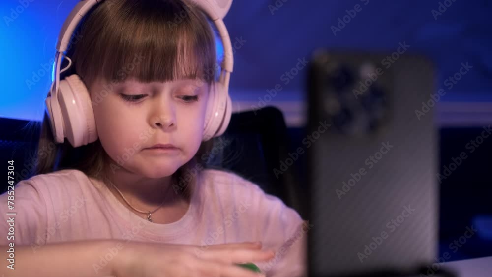 Little girl records a funny video using a smartphone and lamp with light. The white child is