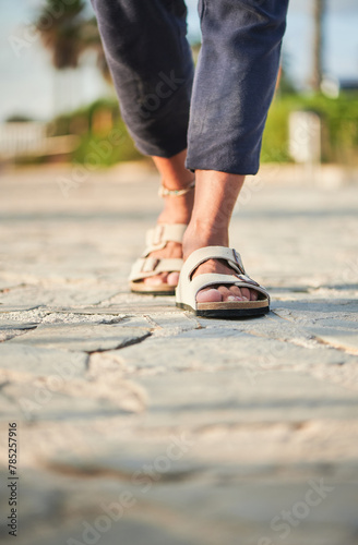 Legs of an unrecognizable trendy man walking with comfortable sandals on his feet on the pier of the marina at sunset on a summer day photo