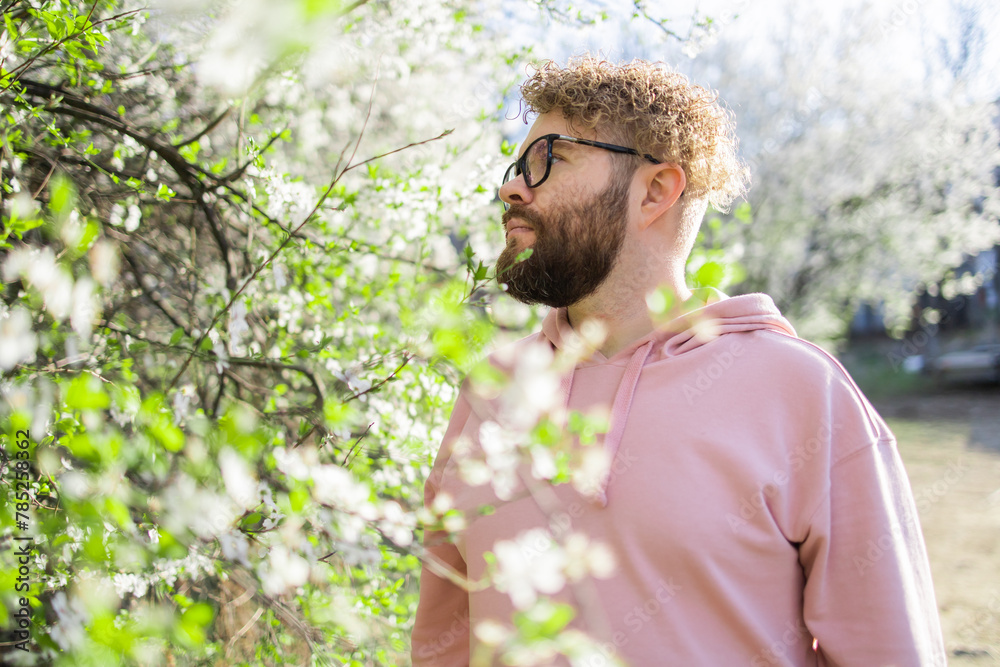 Man with beard and mustache on smiling face near sakura flowers or blooming spring tree. Soft and gentle concept. Bearded man with stylish haircut with flowers on background, close up. Hipster near