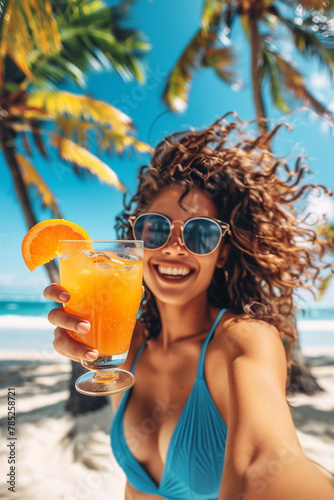 Beautiful young woman with long curly hair and in sunglasses holding glass with summer orange cocktail on a beach. Beach vacation. © Tanya