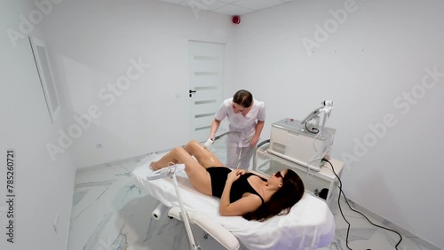 Young woman doing depilation in beauty salon using laser hair removal equipment in modern cosmetology clinic, wide angle. Laser hair removal epilation, waxing, sugaring, electrolysis photo