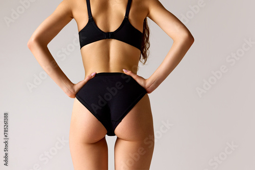 Rear view photo of female body, buttocks against white studio background. Female model posing in lingerie holding hands on hips. Concept of beauty, dieting programs, anti-cellulite, weight loss. Ad