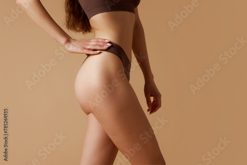 Young slender woman demonstrating her slim figure against sandy background. Girl with well-kept tanned skin. Concept of beauty and health, skin care treatments, spa procedures, depilation. Ad