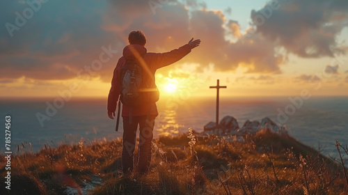 Man standing on hill by cross with sunset backdrop, overlooking horizon. photo