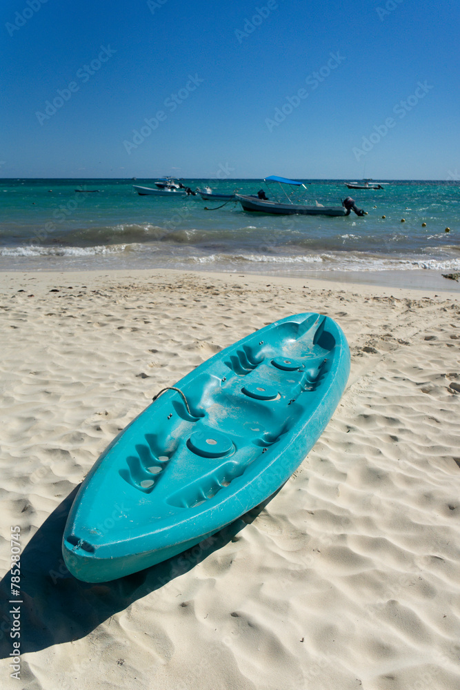 Tropical beach in Mexico with turquoise kayaks on white sand, blue sky and calm sea with boats in the background. Ideal place for vacation sports and relaxation Tropical beach in Mexico with turquoise kayaks on white sand, blue sky and calm sea with boats in the background. Ideal place for vacation sports and relaxation