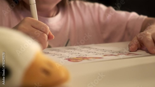 Cute smart preschool 5 years old girl writing homework in exercise copybook, learning letters, sitting at home table. Preparation for school. Home distance education. Children preschool concept. photo