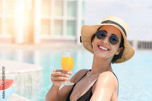 Happy smiling woman in bikini with straw hat relaxing with orange juice at poolside. beautiful female relaxing in summer time. holiday vacation concept