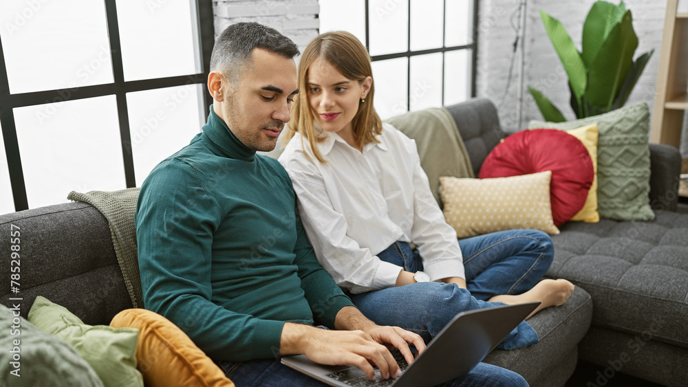 A couple relaxes on a sofa with a laptop, suggesting a cozy, domestic setting in a modern living room. A couple relaxes on a sofa with a laptop, suggesting a cozy, domestic setting in a modern living room.