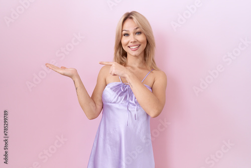 Young caucasian woman wearing lingerie dress amazed and smiling to the camera while presenting with hand and pointing with finger.