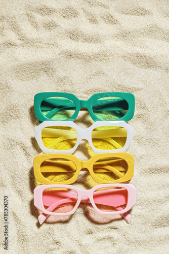 Stylish colored sunglasses on sand background at sunlight, summer fashion collection eyeglasses with colors glass. Summer sale concept in optical store. Top view lifestyle aesthetic photo, copy space