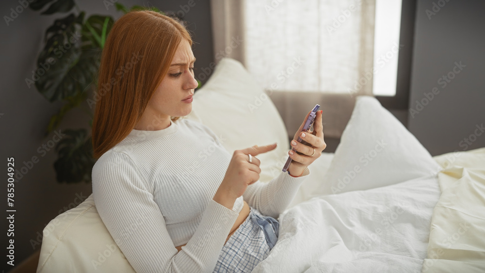 A young woman using a smartphone while sitting on a bed in a well-lit bedroom. A young woman using a smartphone while sitting on a bed in a well-lit bedroom.