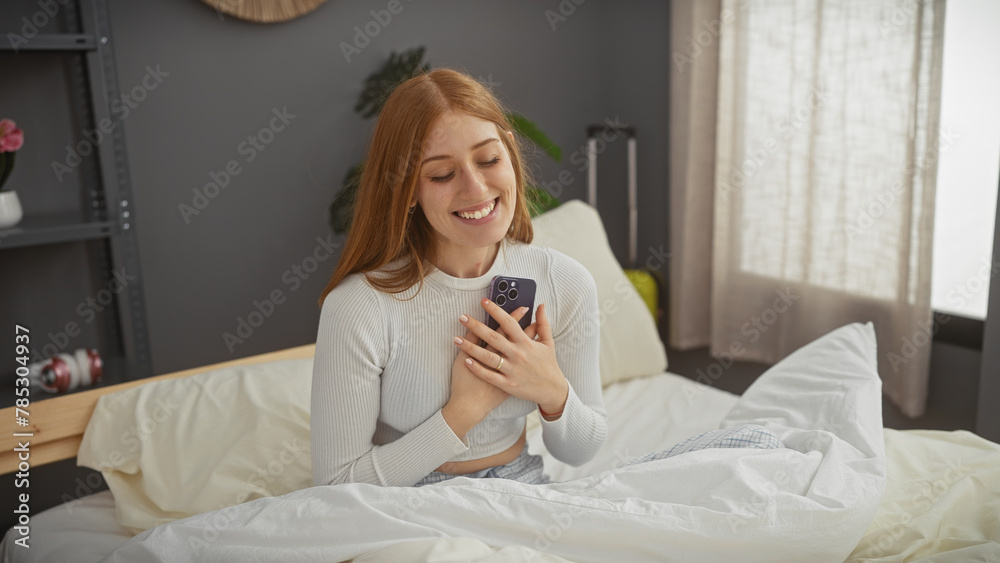 Smiling young woman holding phone in bed, conveying a cozy, happy indoor mood with her casual appearance and modern bedroom setting. Smiling young woman holding phone in bed, conveying a cozy, happy indoor mood with her casual appearance and modern bedroom setting.