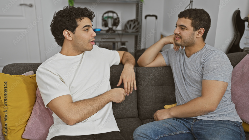 Two men conversing comfortably on a sofa in a modern living room. Two men conversing comfortably on a sofa in a modern living room.