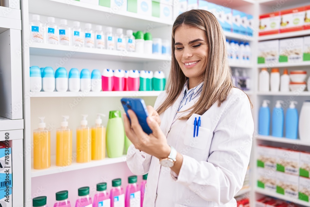 Young beautiful hispanic woman pharmacist using smartphone working at pharmacy
