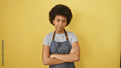 Confident african woman with arms crossed standing against a yellow background wearing a denim apron photo