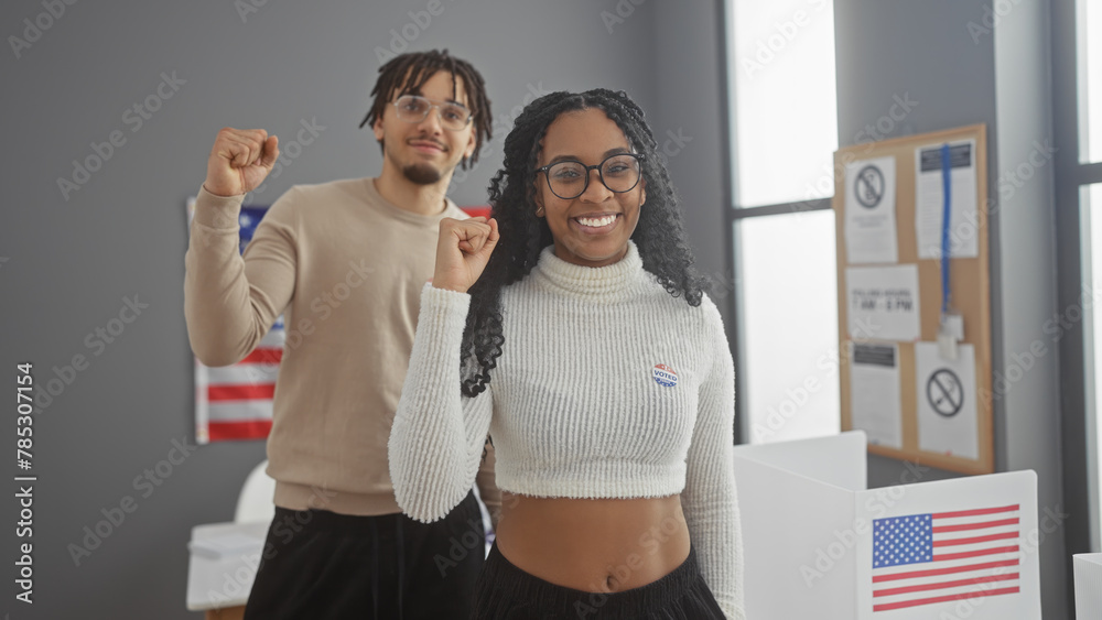 A cheerful man and woman with 'i voted' stickers, raising their fists in unity at an american polling station, symbolizing democratic participation. - obrazy, fototapety, plakaty 