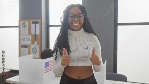 A cheerful woman with glasses giving thumbs up in a polling station with us flags during an election. photo