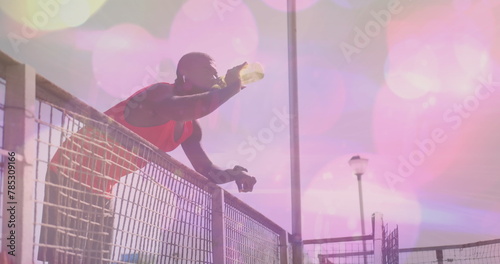 Image of light spots over african american man drinking water at beach photo