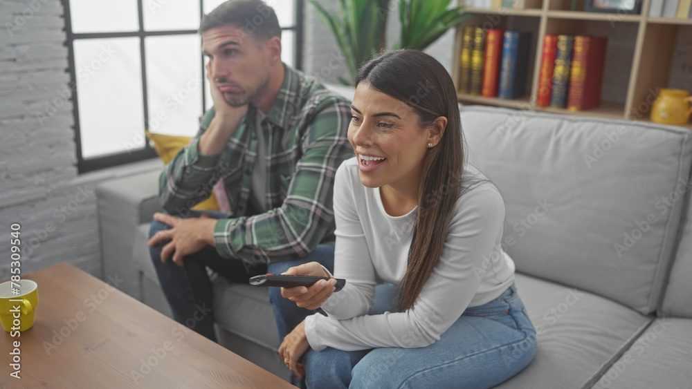 Fototapeta premium A smiling woman and a pensive man sit together on a gray sofa in a modern living room, portraying emotions and relationships.