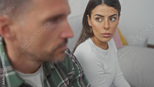 Εκτύπωση καμβά A hispanic couple appears contemplative in their living room, the woman looking anxious alongside her man on the sofa