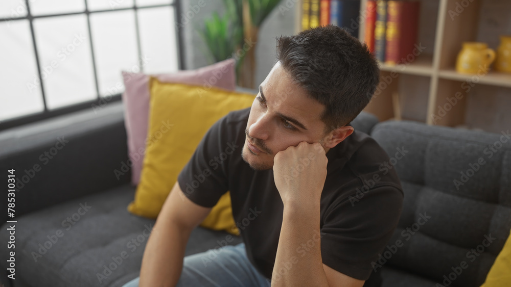 Thoughtful hispanic man with beard sitting in living room looking pensive Thoughtful hispanic man with beard sitting in living room looking pensive