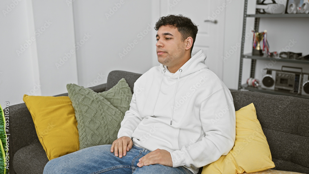 A relaxed young man in a white hoodie lounging on a cozy sofa with vibrant pillows in a modern living room setting.