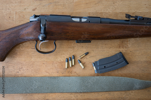 Detail of an old standard .22 caliber bolt action carbine on a wooden table along with bullets and an extended 15 magazine