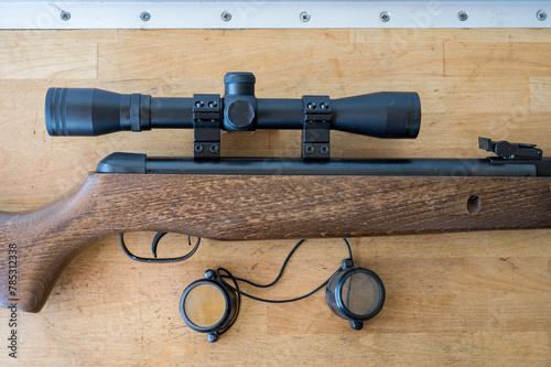 Detail of a light precision air rifle with optical sight on a wooden table. It is a 4.5mm caliber rifle for hunting pigeons.