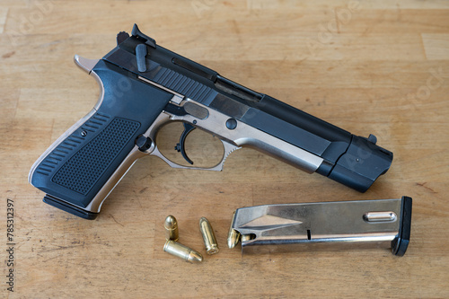 Detail of a nice 9mm police pistol next to a loaded bullet magazine and a few bullets on the wooden table photo