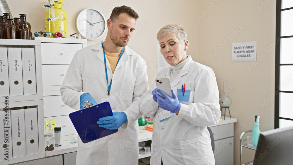 A man and woman in lab coats review data on a smartphone in a bright laboratory setting, portraying professionals at work. A man and woman in lab coats review data on a smartphone in a bright laboratory setting, portraying professionals at work.