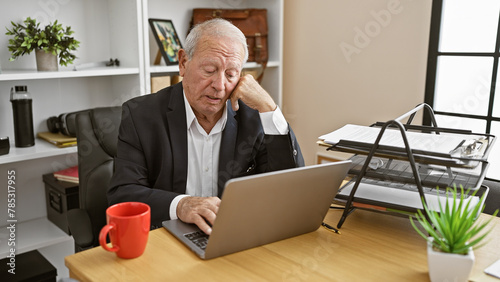 Serious, thoughtful senior man immersed in work, concentrating on business issues via laptop at office desk. a mature, elegant worker focused on success, doubting, crafting ideas and solutions.