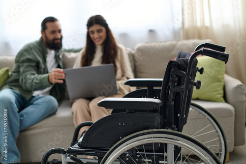 focus on modern wheelchair in front of blurred bearded man and disabled woman looking at laptop