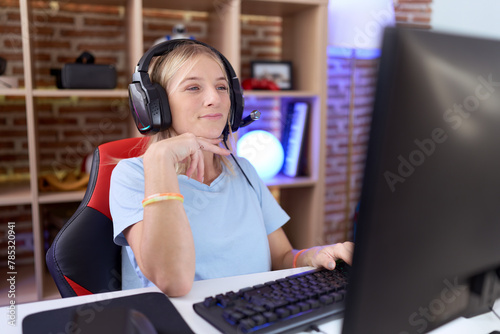 Young caucasian woman playing video games wearing headphones with hand on chin thinking about question, pensive expression. smiling and thoughtful face. doubt concept.