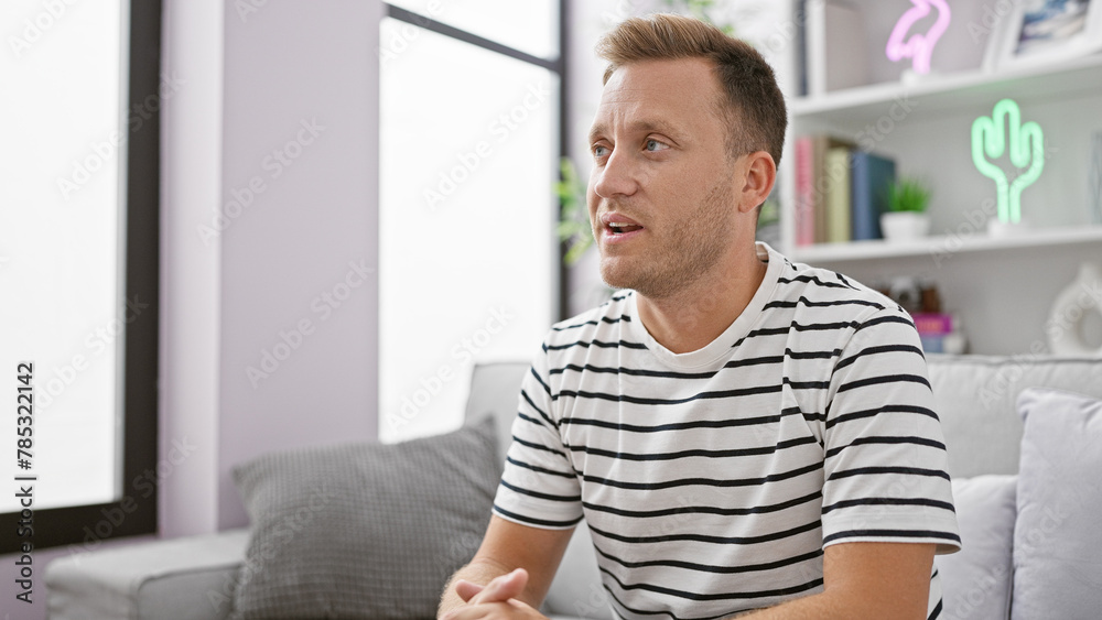 Confident young caucasian man happily resting on his cozy sofa, enjoying the comfort of home with a relaxing smile Confident young caucasian man happily resting on his cozy sofa, enjoying the comfort of home with a relaxing smile