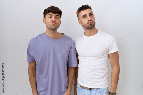 Homosexual gay couple standing over white background looking at the camera blowing a kiss on air being lovely and sexy. love expression.