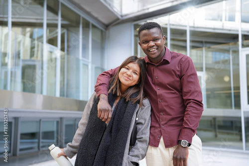 Multi-ethnic couple embracing in the city smiling at camera