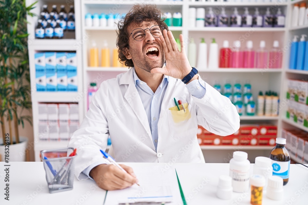 Hispanic young man working at pharmacy drugstore shouting and screaming loud to side with hand on mouth. communication concept.
