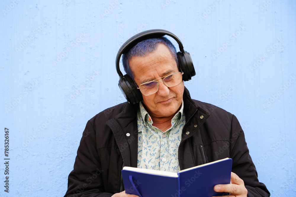Mature man using headphones while reading notebook Mature man using headphones while reading notebook