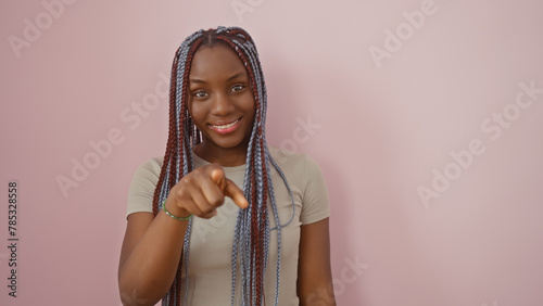 Portrait of a smiling african woman with braids pointing on a pink background