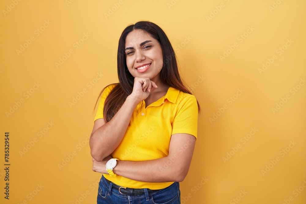 Young arab woman standing over yellow background with hand on chin thinking about question, pensive expression. smiling and thoughtful face. doubt concept. Young arab woman standing over yellow background with hand on chin thinking about question, pensive expression. smiling and thoughtful face. doubt concept.
