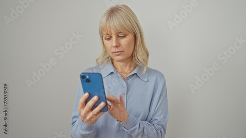 A focused caucasian woman in casual attire uses a smartphone against a plain white background.