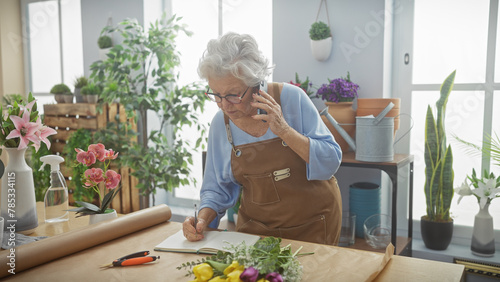 Senior woman florist taking order over phone in flower shop photo