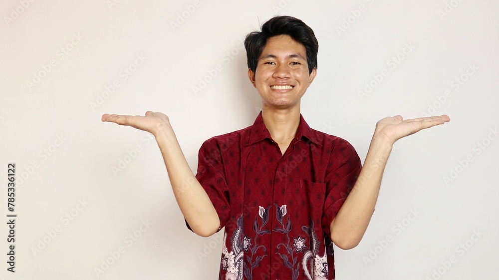 Handsome Asian young man dressed in batik posing with open arms and looking at palms Handsome Asian young man dressed in batik posing with open arms and looking at palms